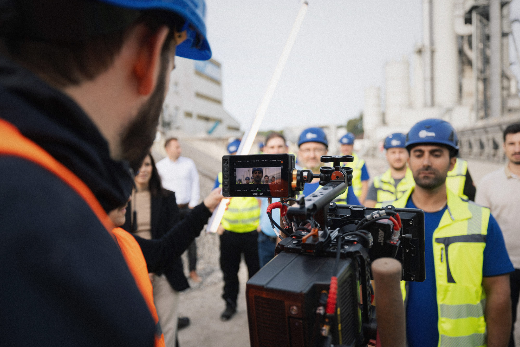 Die Regie von quadratkollektiv aus Nürnberg gibt Anweisungen für ein Gruppenbild auf einer Baustelle. / The director from quadratkollektiv in Nuremberg gives instructions for a group photo on a construction site.